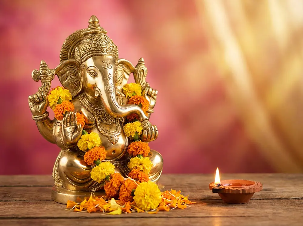 Brass Ganesha idol with marigolds and a diya