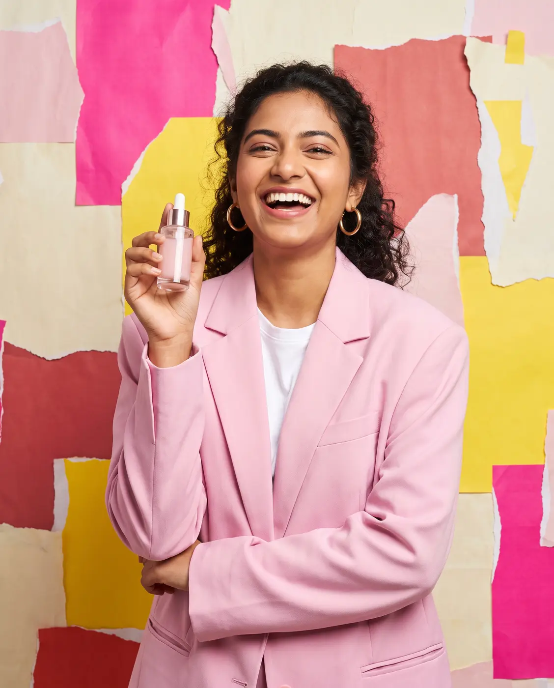 Smiling young woman in a pink blazer holding a serum bottle against a pink and yellow paper wall
