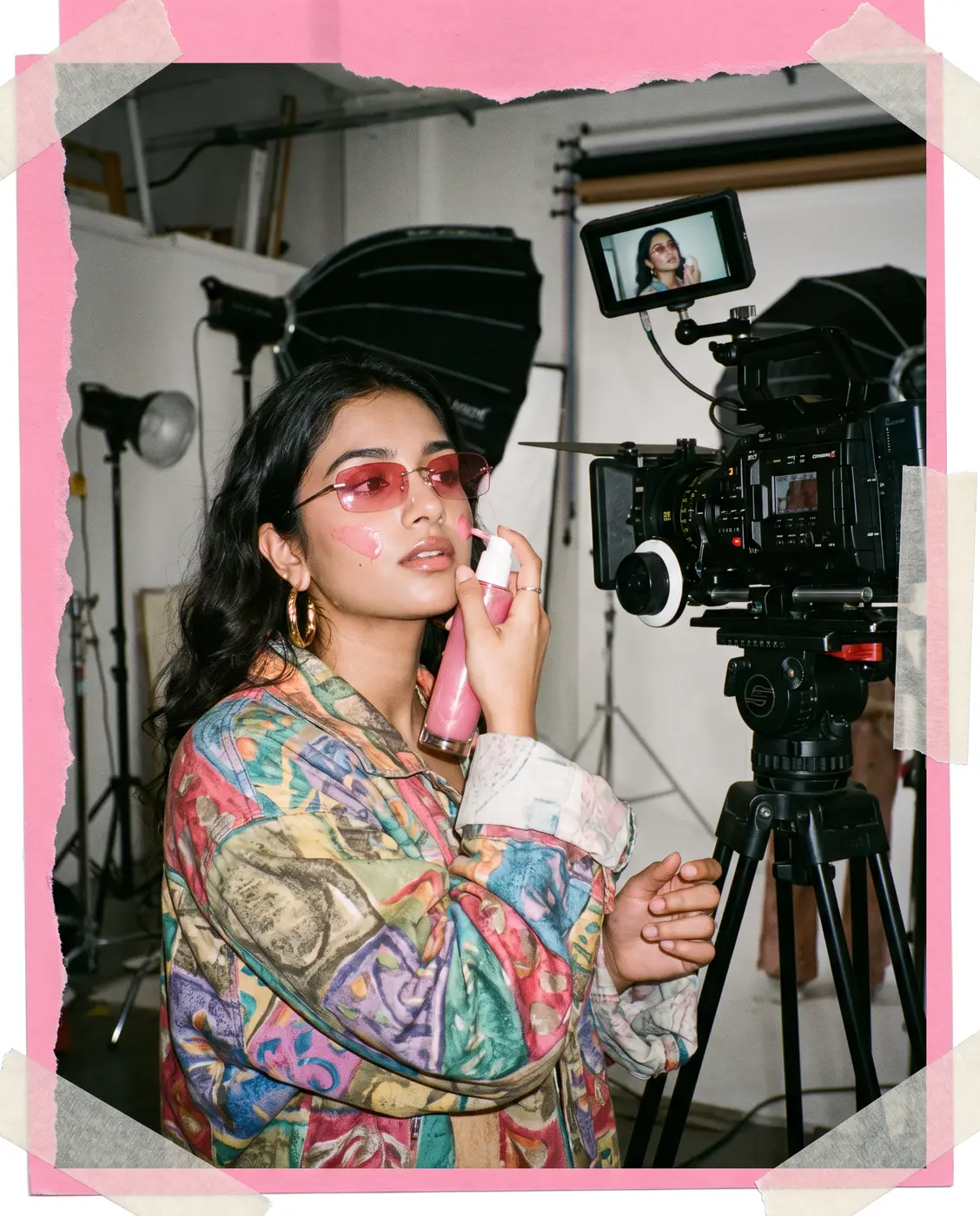 Model in pink sunglasses holding a skincare bottle on a studio set